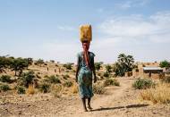 Une femme qui porte un bidon d’eau usé par le temps dans le désert (Crédit : Alex.I)